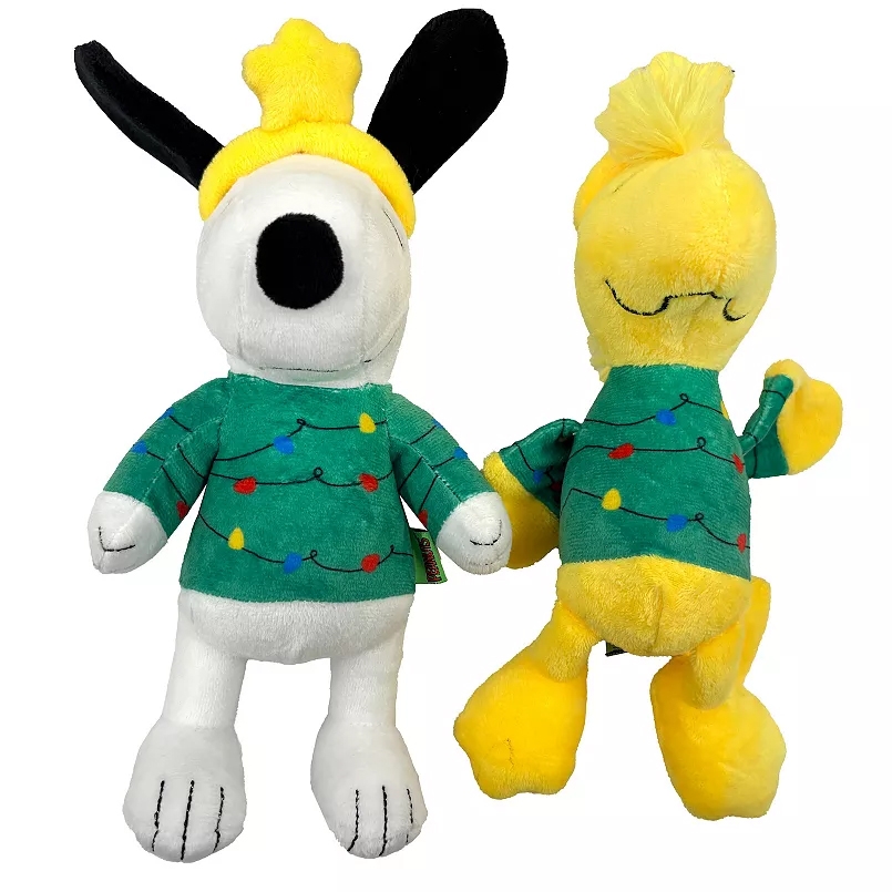A 2-piece Peanuts dog toy set featuring plush characters with green holiday sweaters adorned with colorful string lights. One toy is a white dog with a yellow star hat, and the other is a yellow bird.