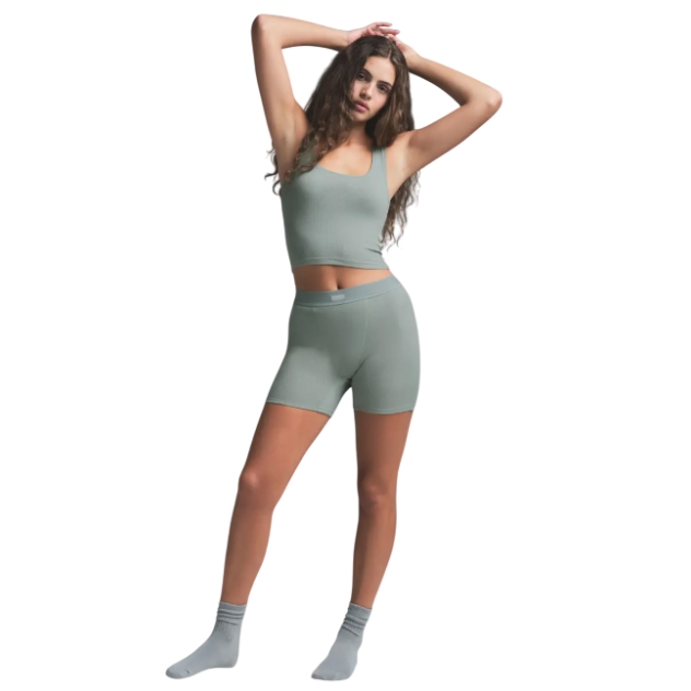 A woman is wearing a light green ribbed tank top and matching high-waisted boxer shorts with a fitted, seamless design, paired with green socks. The outfit emphasizes comfort and a snug fit, suitable for casual or lounge wear.