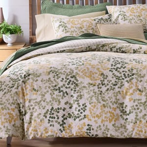 Bedding set featuring a nature-inspired design with green and yellow leaf patterns, complemented by coordinating pillows and a green quilted accent.