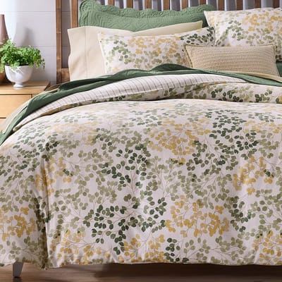 Bedding set featuring a nature-inspired design with green and yellow leaf patterns, complemented by coordinating pillows and a green quilted accent.