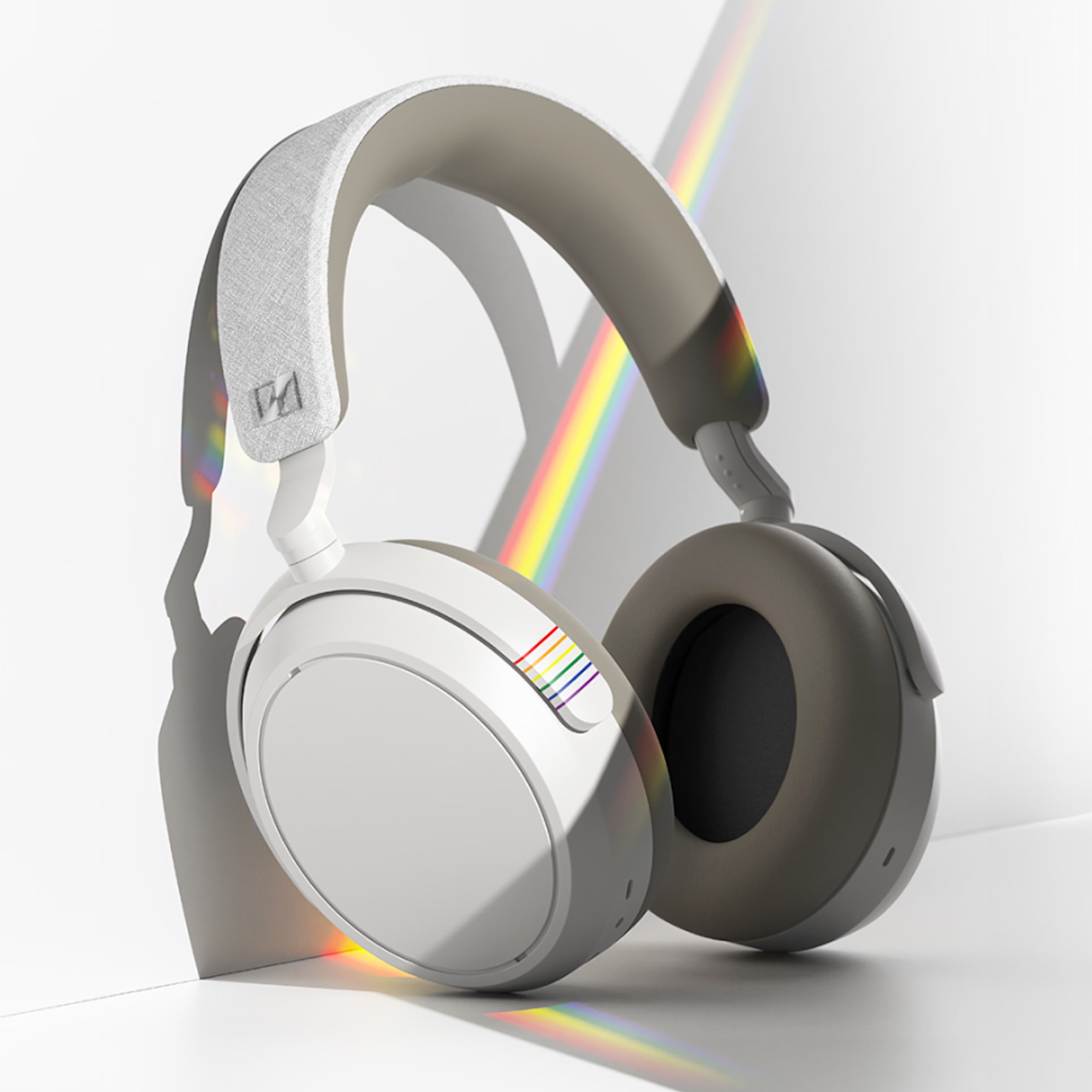 White over-ear headphones with a rainbow accent on the headband and ear cup, reflecting a pride theme.