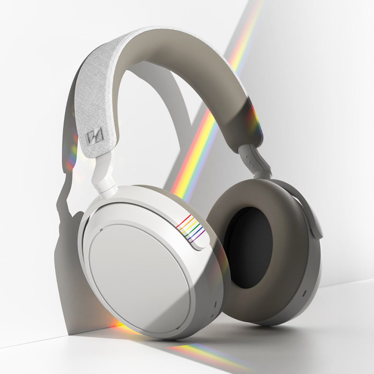White over-ear headphones with a rainbow accent on the headband and ear cup, reflecting a pride theme.