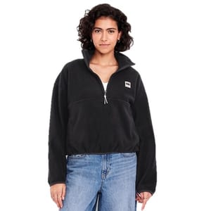 A woman is wearing a black half-zip fleece jacket with a logo on the chest, paired with blue jeans.