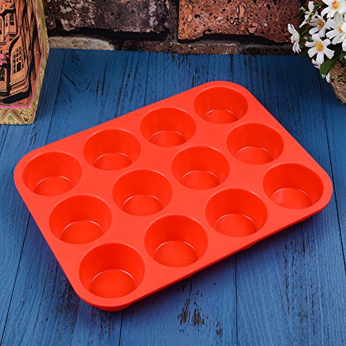 A red silicone muffin tin with 12 round cavities for baking, placed on a blue wooden surface next to white flowers.
