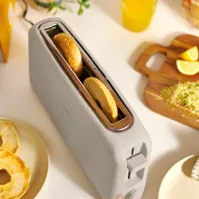 A toaster with a long, wide slot fitting two slices side-by-side, surrounded by toasted bagels and lemons on a cutting board.