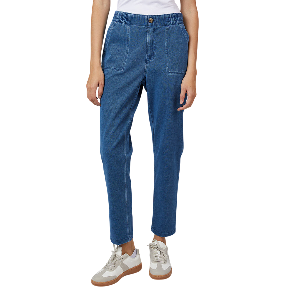 A person is wearing blue denim jogger pants paired with white and beige sneakers. The pants feature an elastic waistband with a button closure and large front pockets.