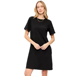 A woman is wearing a simple black T-shirt dress with a round neckline and short sleeves, complemented by a thin necklace.