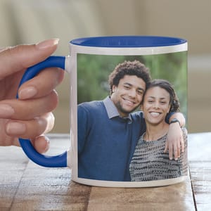 A white mug with blue trim and handle displays a photo of two people smiling and embracing, printed on the side.