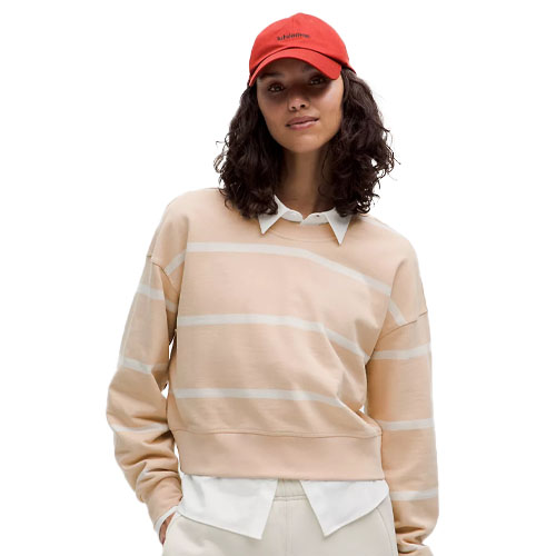 A woman is wearing a beige and white striped sweater layered over a white collared shirt, paired with light pants and a red baseball cap.