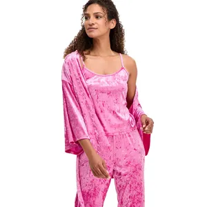 A person in a pink crushed velvet pajama set with a cami top, matching pants, and a draped robe over one shoulder.