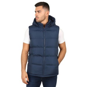 A man wears a navy blue hooded puffer vest over a white T-shirt, paired with dark blue jeans.