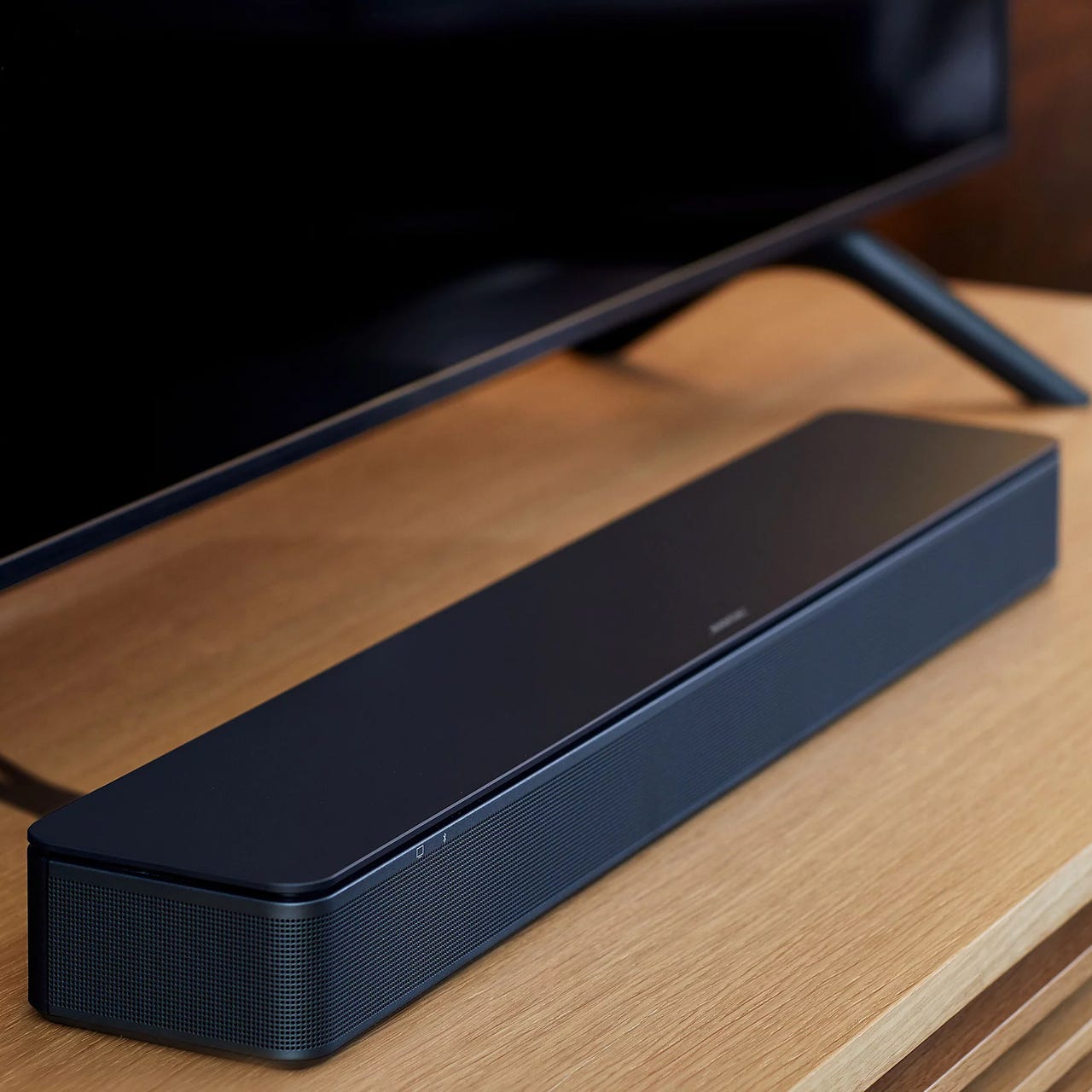 A black soundbar placed beneath a television on a wooden surface.