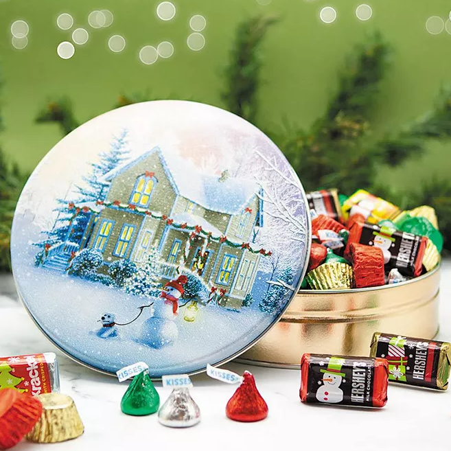 A festive tin decorated with a snow-covered house scene contains an assortment of 50 pieces of wrapped Hershey's chocolates, including Kisses and miniatures.