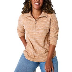 A smiling person is wearing a light orange long-sleeve pullover with a quarter-zip collar and light blue jeans.