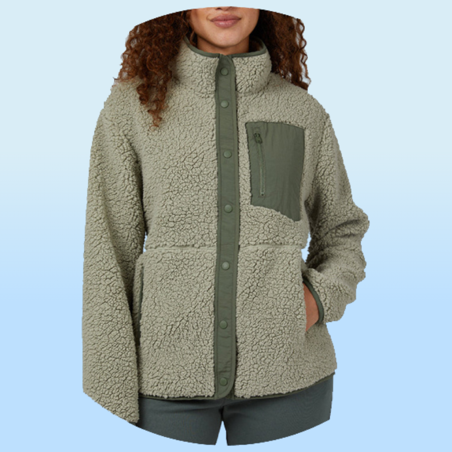 A woman wearing a light green, button-up sherpa fleece jacket with a high collar, featuring a contrasting green chest pocket with a zipper and side pockets.