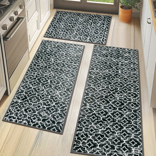 Set of three black and white patterned kitchen rugs with a geometric design arranged on a light wood floor.