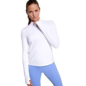 A woman is wearing a white long-sleeve pullover top and light blue leggings.