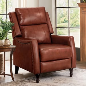 A brown leather recliner with nailhead trim and dark wooden legs is positioned near a wooden side table holding a plant and decorative items, set in a room with large windows.