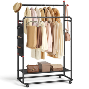 A black metal garment rack with wheels features dual hanging rods for jackets and shirts, side storage pockets, a bottom shelf with bags and boxes, and hooks for hats and a bag. Clothing items are in neutral tones.