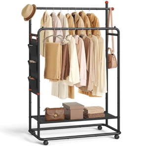 A black metal garment rack with wheels features dual hanging rods for jackets and shirts, side storage pockets, a bottom shelf with bags and boxes, and hooks for hats and a bag. Clothing items are in neutral tones.