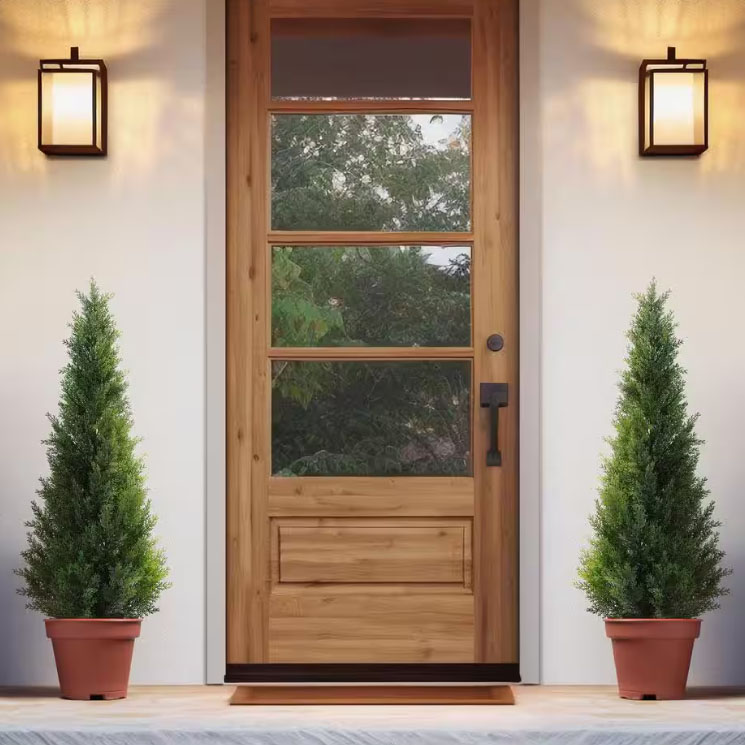 A pair of 4-foot outdoor faux topiaries in terracotta pots, featuring dense, lush greenery shaped into a conical form. They are placed symmetrically on either side of a wooden door, flanked by modern wall sconces.