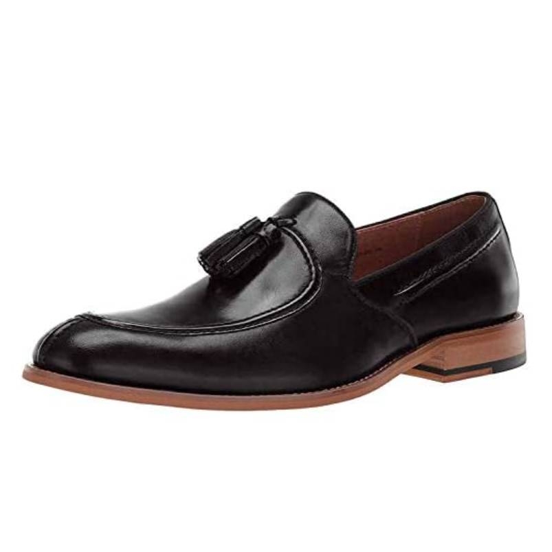 A black leather loafer with a tassel detail, featuring a brown sole and a low heel.