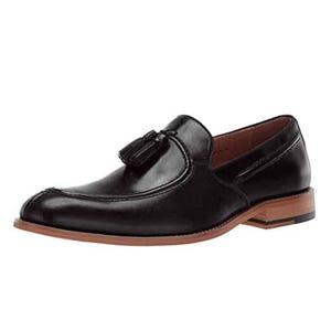 A black leather loafer with a tassel detail, featuring a brown sole and a low heel.