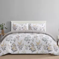 A bed set with a floral-patterned comforter and matching pillowcases in shades of grey, yellow, and white, accessorized with a small wooden side table holding a potted plant.