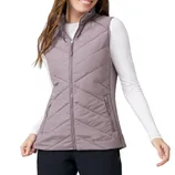 A woman wears a light mauve quilted vest with a high collar and two zippered pockets, paired with a white long-sleeve shirt and black pants.