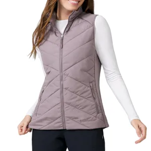 A woman wears a light mauve quilted vest with a high collar and two zippered pockets, paired with a white long-sleeve shirt and black pants.