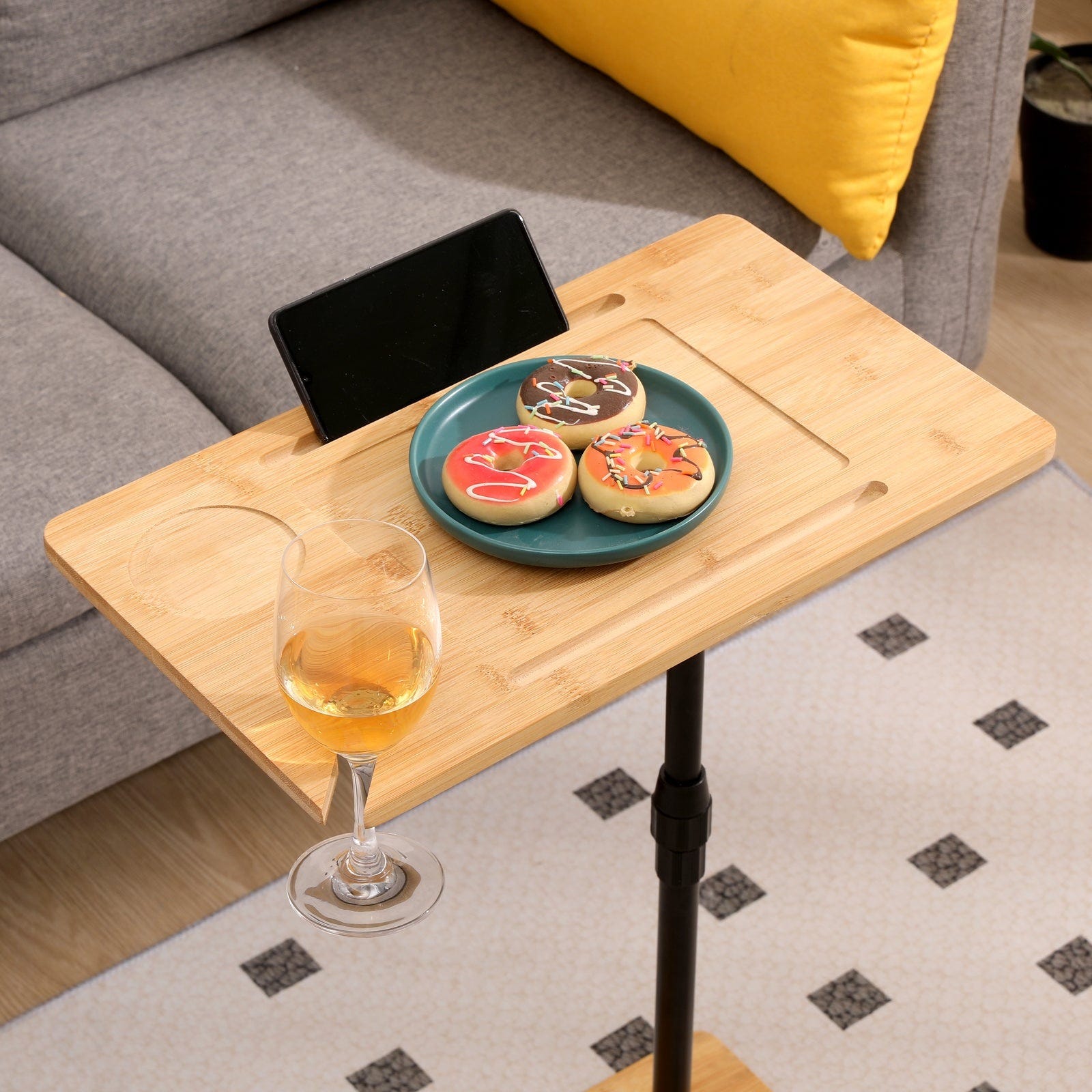 A small wooden side table holds a plate with three decorated cookies, a glass of white wine, and a tablet propped up in a slot.