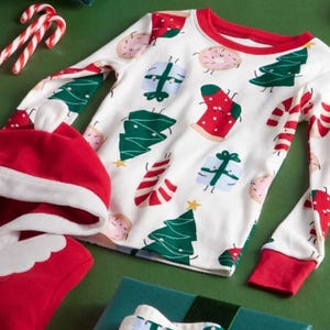 A Christmas-themed pajama top with festive designs like trees, candy canes, gifts, and stockings, accompanied by a red and white Santa hat.