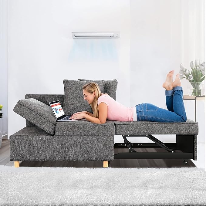 A woman is lying on a grey sectional sofa with adjustable backrests, using a laptop placed on one of the sofa segments.