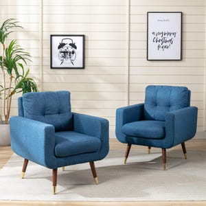Two tufted armchairs with deep blue upholstery and angled wooden legs are shown in a well-decorated room with framed art on the wall.