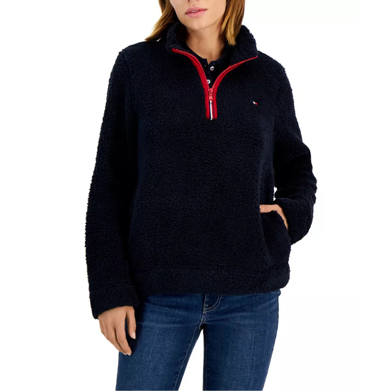 A navy Sherpa pullover jacket with a plush texture, featuring a red half-zip closure and a small logo on the chest, paired with blue jeans.