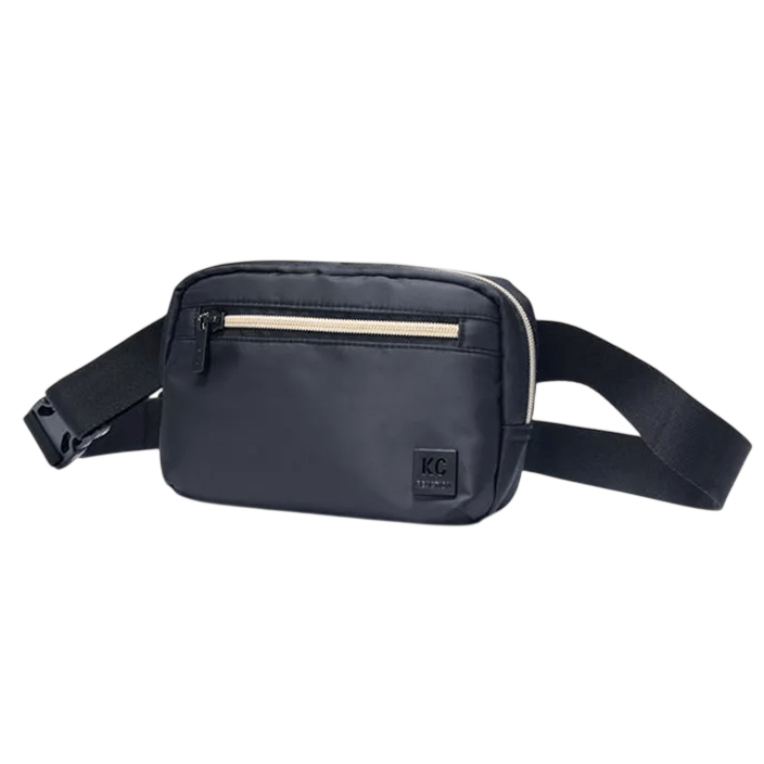 A black crossbody bag with a beige zippered front pocket and adjustable strap, featuring a small \“KC\“ logo.