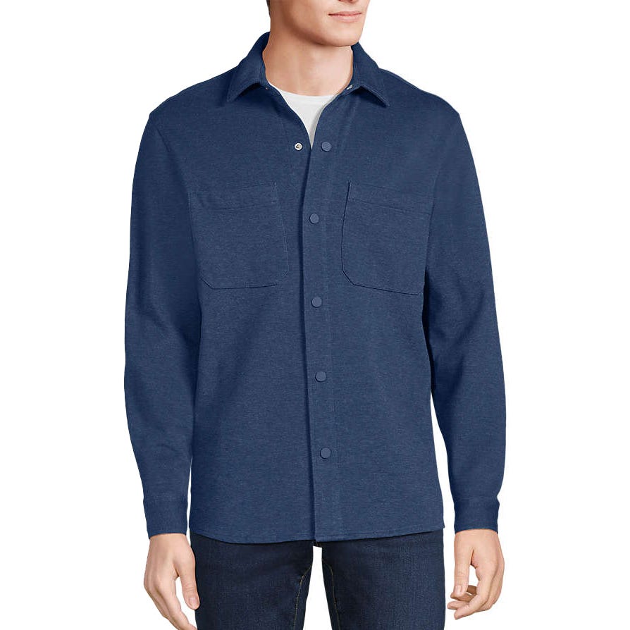 A man wears a navy blue long-sleeve button-up shirt with two front chest pockets over a white undershirt, paired with dark jeans.