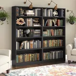 A black bookshelf with six shelves is filled with an assortment of books. Decorative items like a globe, coral sculptures, and a wall-mounted lamp enhance its appearance, and a floral-patterned rug and white armchair are positioned nearby for a cozy reading nook.