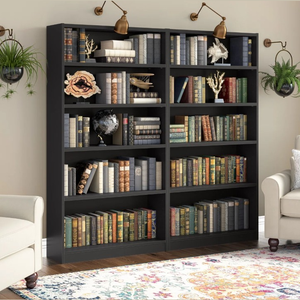 A black bookshelf with six shelves is filled with an assortment of books. Decorative items like a globe, coral sculptures, and a wall-mounted lamp enhance its appearance, and a floral-patterned rug and white armchair are positioned nearby for a cozy reading nook.