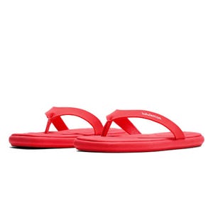 Red flip-flops with a thin strap and a cushioned sole, featuring the \“lululemon\“ logo on the strap.