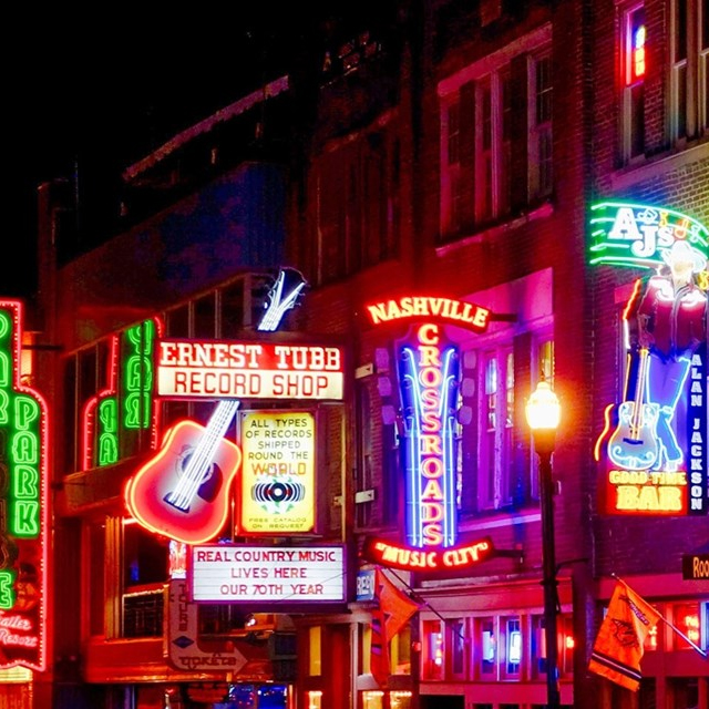 Neon signs for Ernest Tubb Record Shop, Nashville Crossroads Music City, and a bar featuring Alan Jackson, showcasing music and nightlife in a vibrant urban setting.