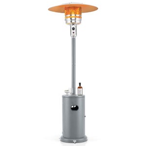 A freestanding outdoor patio heater with a gray base, topped by a wide metal reflector. It includes a shelf with a bottle and other items placed on it.