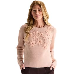 A woman wearing a light pink sweater featuring textured flower designs on the chest area, paired with dark trousers.
