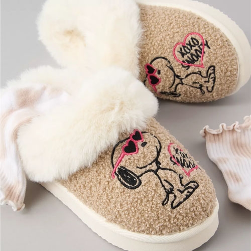 A pair of beige fuzzy slippers with heart and skull embroidery and fluffy white cuffs.