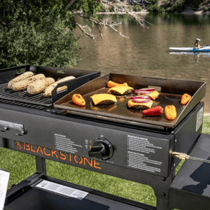 Blackstone outdoor grill with burgers and vegetables on half griddle and half grill surface, next to a river with a person kayaking.