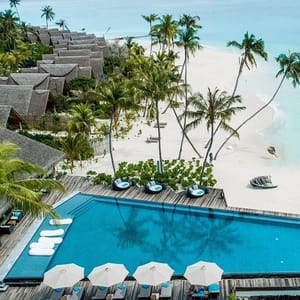 A tropical resort with a swimming pool, beachside villas, palm trees, and a white sandy beach.