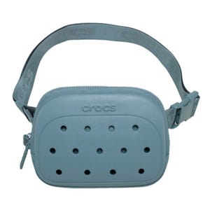A light blue crossbody bag with a design resembling Crocs shoes, featuring ventilation holes and an adjustable strap with the brand name \“Crocs\“ embossed on it.