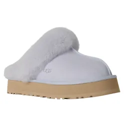 A white UGG slipper with a fluffy trim, featuring a thick beige sole and the UGG logo embossed on the side.