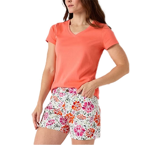 A woman wears a coral t-shirt paired with white shorts featuring a vibrant floral print in pink and orange shades.