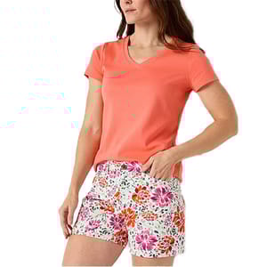 A woman wears a coral t-shirt paired with white shorts featuring a vibrant floral print in pink and orange shades.